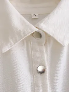 Close-up of white denim jacket featuring a classic collar and silver metal buttons