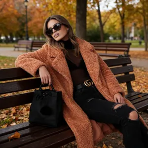 Detail view of warm caramel teddy bear coat styled with black turtleneck and ripped jeans