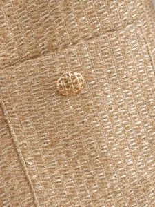 Makro-Detail des goldenen Tweed-Jackenstoffes mit Metallfaden und gewebtem Knopf