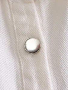 Detailed close-up of white denim jacket fabric texture and silver-tone metal button