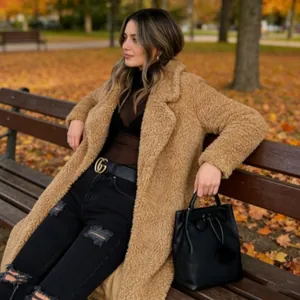 Stylish woman in long camel teddy coat sitting on park bench in autumn