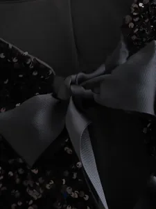 Close-up of black sequined jacket detail featuring a large grosgrain ribbon bow