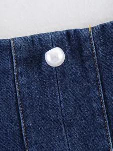 Gros plan d'un bouton de perle blanche sur du denim bleu avec des surpiqûres orange