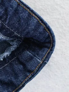 Gros plan d'un haut en denim bleu avec coutures jaunes et détails frangés