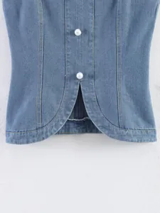 Gros plan d'un gilet en jean bleu avec boutons perlés et ourlet courbé élégant.