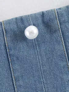 Gros plan d'un haut en jean avec bouton en perle blanche et coutures contrastées chic