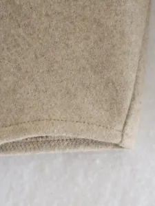 Detailaufnahme einer beige Wolljacke, die hochwertige Stofftextur und Nähte zeigt.