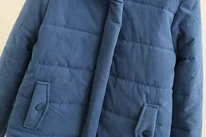 Close-up detail showing the quilted texture and flap pockets of a blue puffer jacket