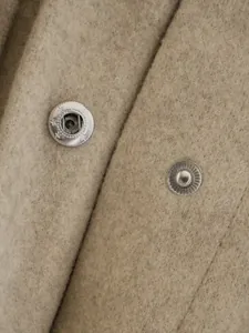 Detailansicht der silbernen Druckknöpfe mit Sternen auf einem dicken beigen Wollmantel