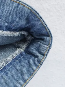 Détail macro montrant les coutures contrastées et le surjet intérieur du haut en denim