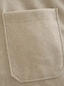 Detailansicht eines beigefarbenen Wollmantels mit einer großen Tasche und feinen Nähten