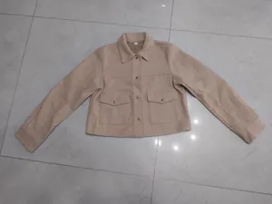 Dettaglio di una giacca corta in lana beige con colletto a camicia e tasche frontali.