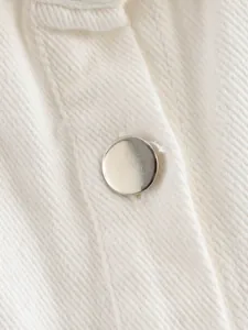 Macro view of a smooth silver metallic button on premium white denim textured fabric