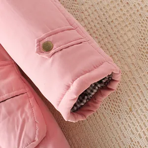 Detaillierte Nahaufnahme des Ärmels eines rosa gesteppten Wintermantels mit Bronzeknopf