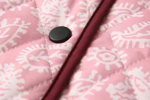 Close-up of quilted floral jacket featuring black snap button and burgundy piping