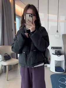 Frau in einer kurzen schwarzen Winter-Steppjacke mit Stehkragen und lila Hose.