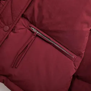 Nahaufnahme des silbernen Reißverschlusses und der Textur einer weinroten Steppjacke.