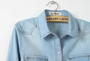 Gros plan détaillé du col et des poches d'une chemise en jean bleu clair avec surpiqûres.