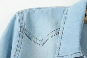 Gros plan de l'épaule d'une chemise en jean montrant des coutures marron et la texture.
