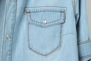 Gros plan de la poche et du bouton-pression en métal sur la chemise en jean bleu clair femme