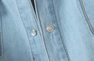 Gros plan sur les boutons-pression et les coutures brunes d'une chemise en jean bleu clair