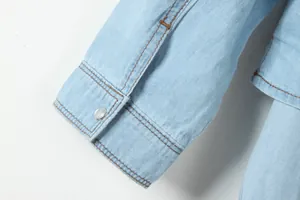 Gros plan détaillé du poignet d'une chemise en jean bleu clair avec des coutures soignées.