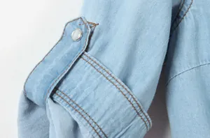 Détail montrant la texture et le bouton pression nacré d'une manche de chemise en jean