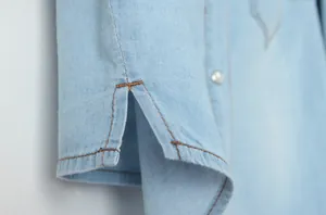 Gros plan de la manche d'une chemise en jean bleu clair avec fente et coutures orange