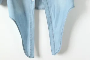Gros plan sur l'ourlet incurvé avec double couture d'une chemise en jean bleu clair