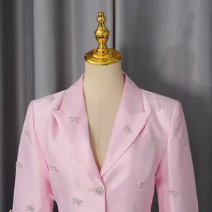 Detail of pink satin blazer featuring rhinestone bow accents and a crystal flower button.