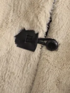 Λεπτομέρεια από το μαύρο κούμπωμα σε μπεζ παλτό από συνθετική γούνα κουνελιού