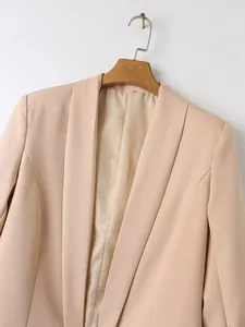 Detailopname van een minimalistische beige blazer met sjaalkraag aan een houten hanger