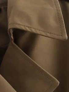 Close-up of premium khaki trench coat fabric showing detailed stitching and twill texture