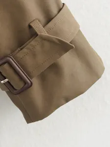 Detailed close-up of a khaki trench coat sleeve cuff featuring a stylish brown buckle strap.