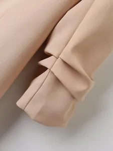 Detailopname van een perzikkleurige blazer met modieuze geplooide manchetten en textuurstof.