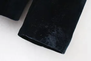 Primo piano del polsino di un blazer in velluto verde scuro con trama morbida del tessuto.