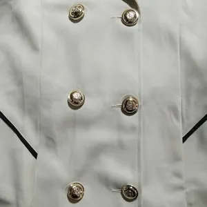Gedetailleerde close-up van de gouden leeuwenkopknopen op een witte dames trenchcoat.