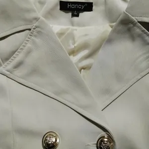 Detailopname van een crèmekleurige blazer met reverskraag en gouden reliëfknopen