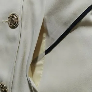 Detail van een witte trenchcoat zak met zwarte bies en een luxe metalen knoop afwerking