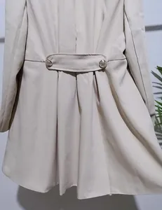 Detailweergave van de rug van een beige trenchcoat met sierstrip en knoopdetail.