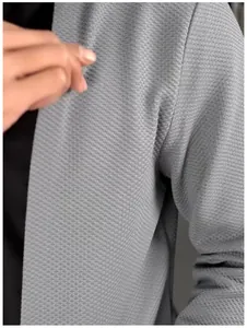 Gros plan du tissu texturé en nid d'abeille gris sur un cardigan en tricot