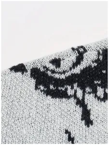 Nahaufnahme der hochwertigen Strickstruktur und des Augenmusters eines schwarz-grauen Pullovers.