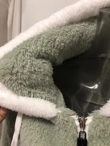 Macro detail of a green plush fleece hoodie showing soft white lining and silver zipper