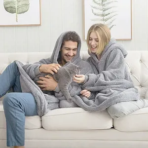 Couple wearing grey oversized fuzzy wearable blankets sitting on a sofa with a cat