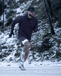Action-Shot eines Mannes beim Laufen in einem lila Sport-Hoodie auf einem Schneeweg