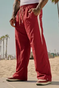 Red men's loose casual trousers with white side stripe shown in a sunny beach setting