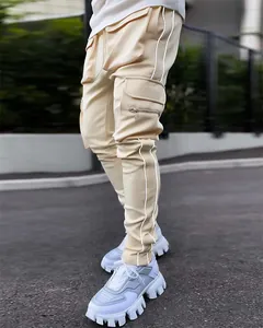 Close-up of men's beige cargo pants with reflective stripes and multi-pocket utility design.