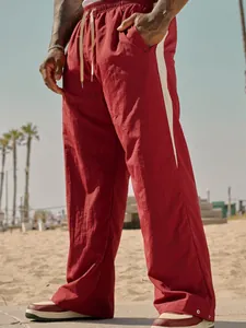 Loose-fit men's red casual trousers with stylish white side stripes on a sunny beach