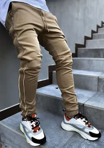 Detail view of khaki joggers featuring white reflective stripes and side zippers.