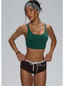 Athletic woman wearing dark green sports bra and brown mini shorts in studio setting